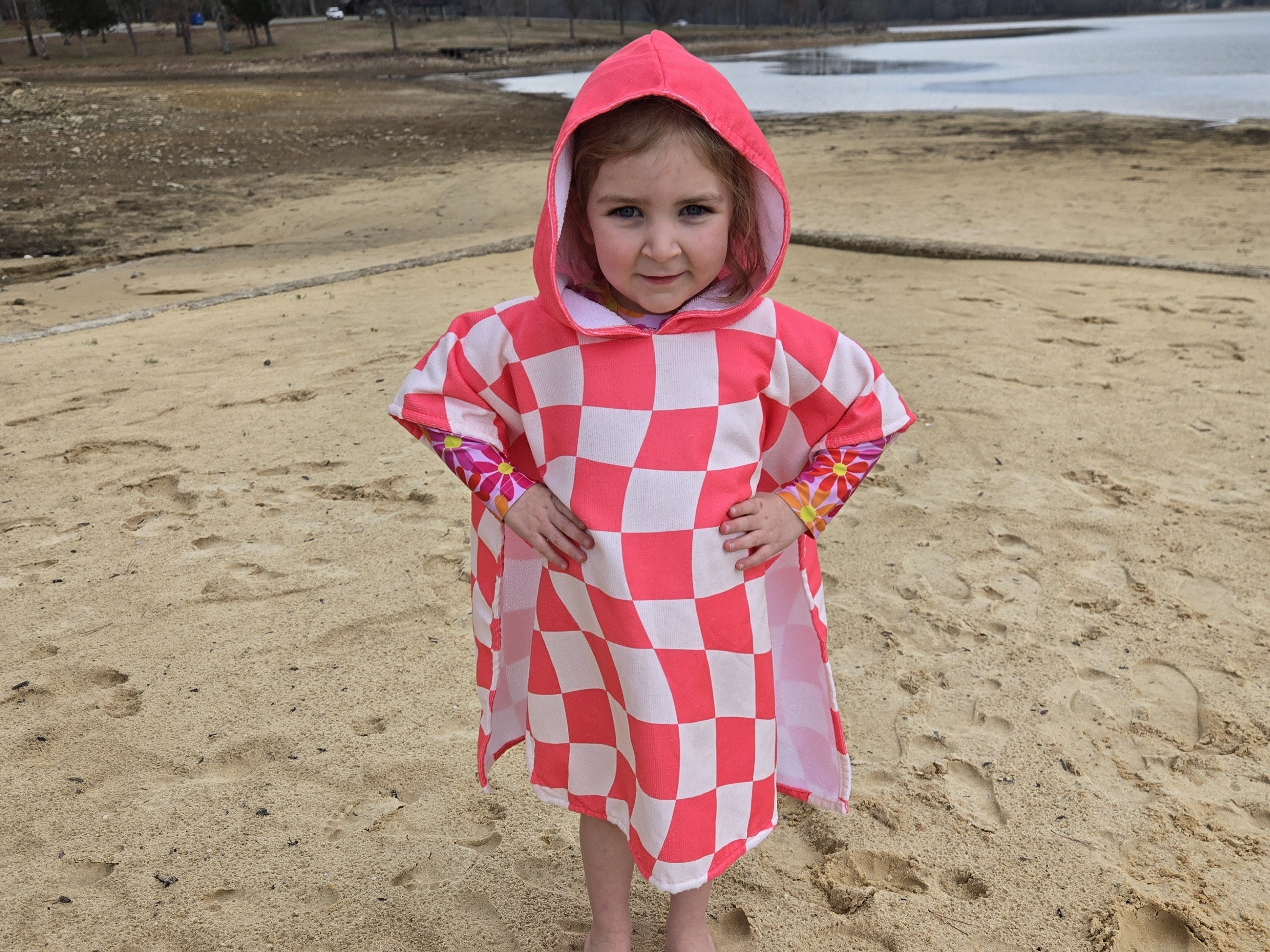 A little girl wearing a pink and white checkered hooded towel at the lake