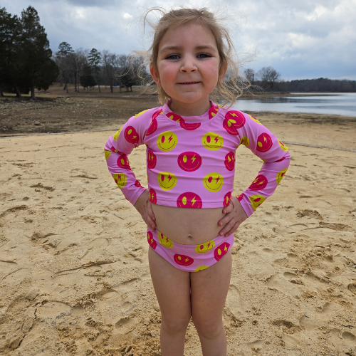 Girl in pink smiley crop top swimsuit on sandy shore