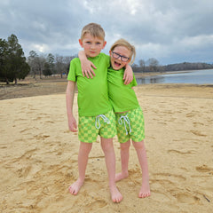 Two boys front view wearing green checkered swim trunks and rash guard set