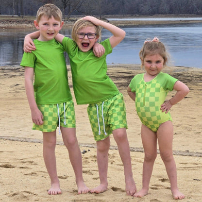 Two boys and a girl wearing neon green checkered swimsuits at the beach